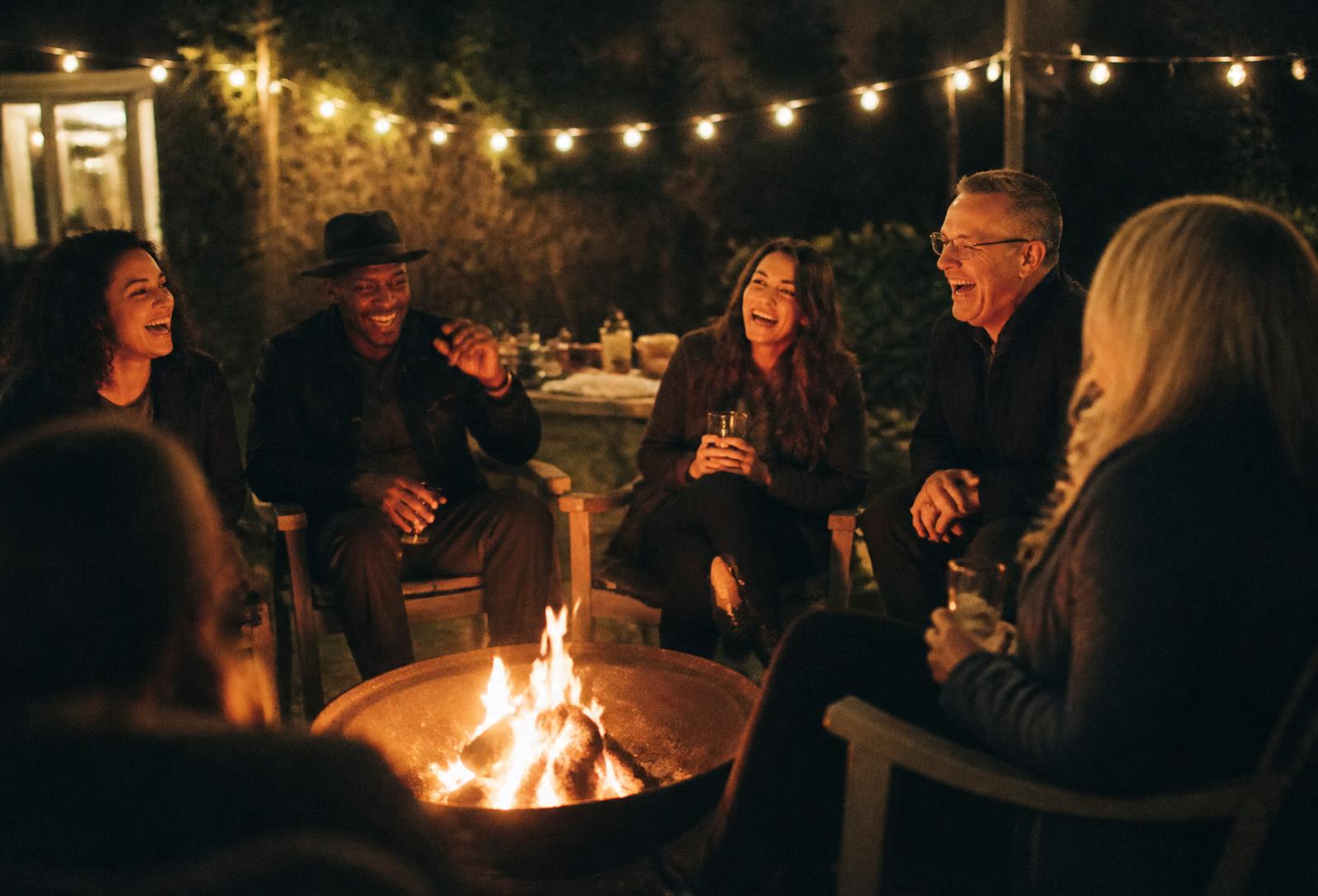 Friends laughing around a backyard fire at night
