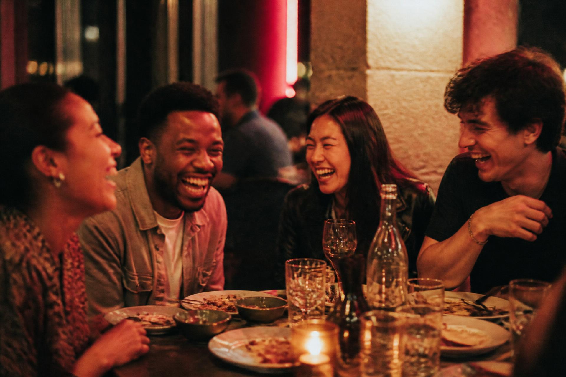 Friends laughing together at a restaurant table late at night